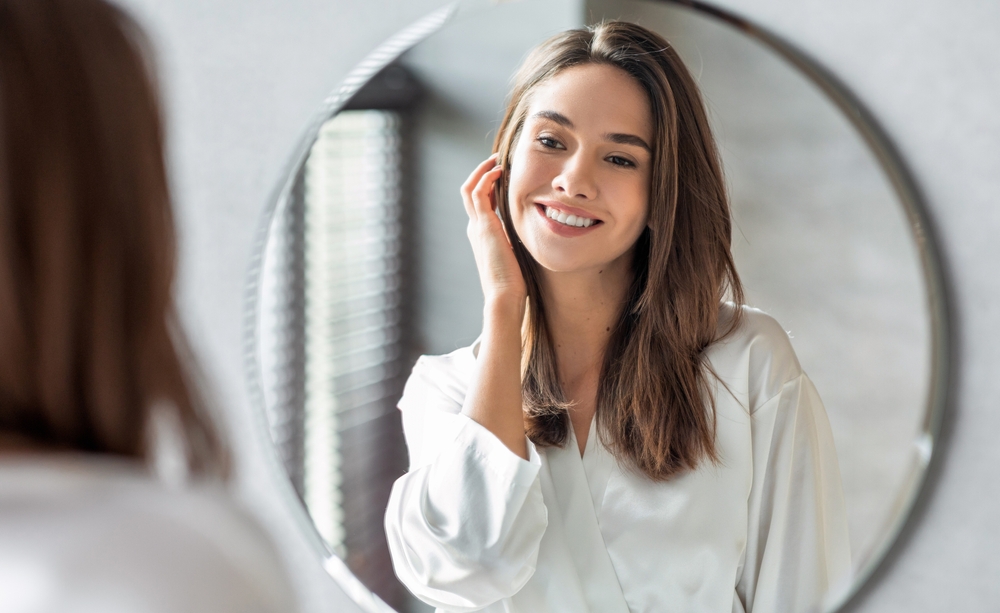 Woman looking at her face in the mirror after dermaplaning in Scarsdale, NY