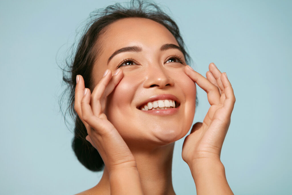Smiling woman touching her cheeks, highlighting smooth, even-looking skin after facial rejuvenation treatments.